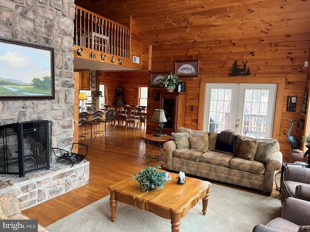 living room with french doors, a fireplace, wooden walls, wood finished floors, and high vaulted ceiling