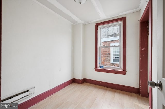 empty room featuring light wood-type flooring, a baseboard radiator, and baseboards