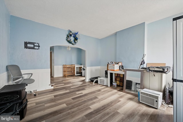 home office featuring arched walkways, wainscoting, a textured ceiling, and wood finished floors