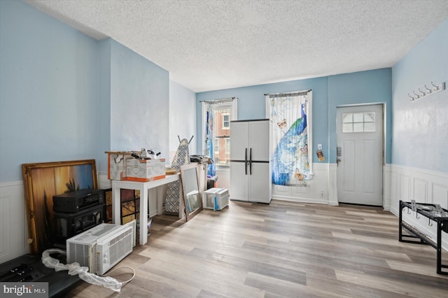 entrance foyer with light wood-type flooring, a wainscoted wall, and a textured ceiling