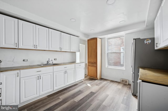 kitchen featuring visible vents, freestanding refrigerator, white cabinets, a sink, and light wood-type flooring