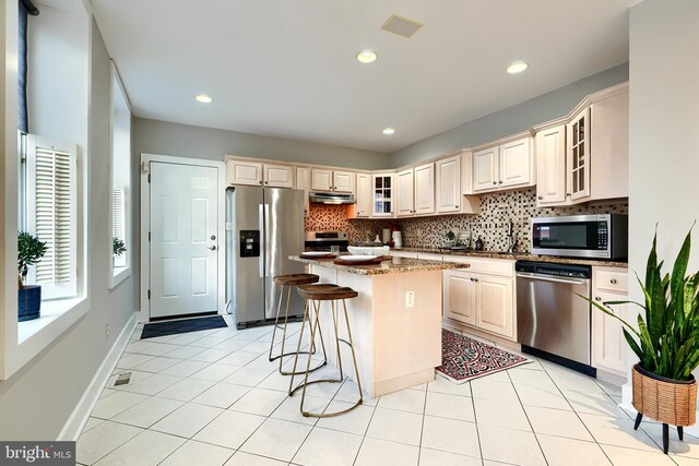 kitchen featuring appliances with stainless steel finishes, a center island, a kitchen bar, decorative backsplash, and cream cabinetry