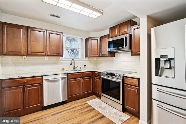 kitchen with light stone counters, sink, stainless steel appliances, and light hardwood / wood-style floors