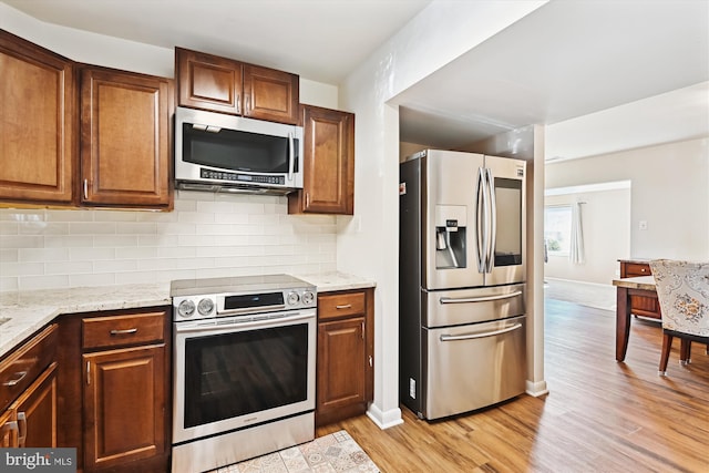 kitchen with stainless steel appliances, light stone countertops, light hardwood / wood-style floors, and backsplash