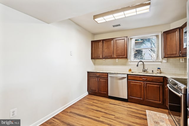 kitchen with sink, appliances with stainless steel finishes, light stone countertops, decorative backsplash, and light wood-type flooring