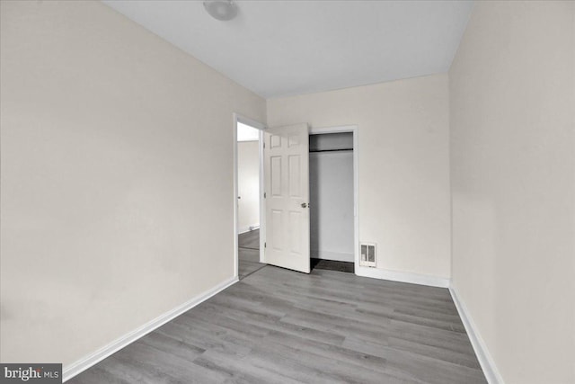 unfurnished bedroom with baseboards, wood finished floors, visible vents, and a closet