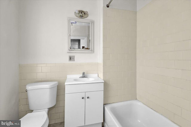 bathroom with a wainscoted wall, vanity, tile walls, toilet, and bathing tub / shower combination