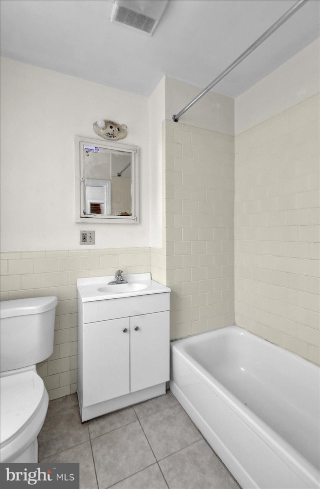 full bathroom with tile walls, visible vents, toilet, tile patterned floors, and a wainscoted wall