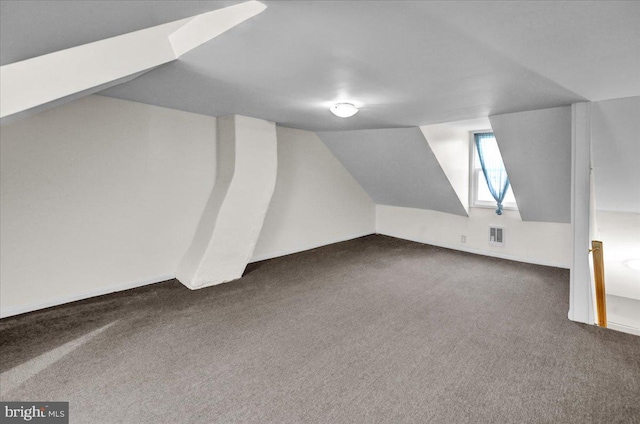 additional living space with visible vents, dark colored carpet, and vaulted ceiling