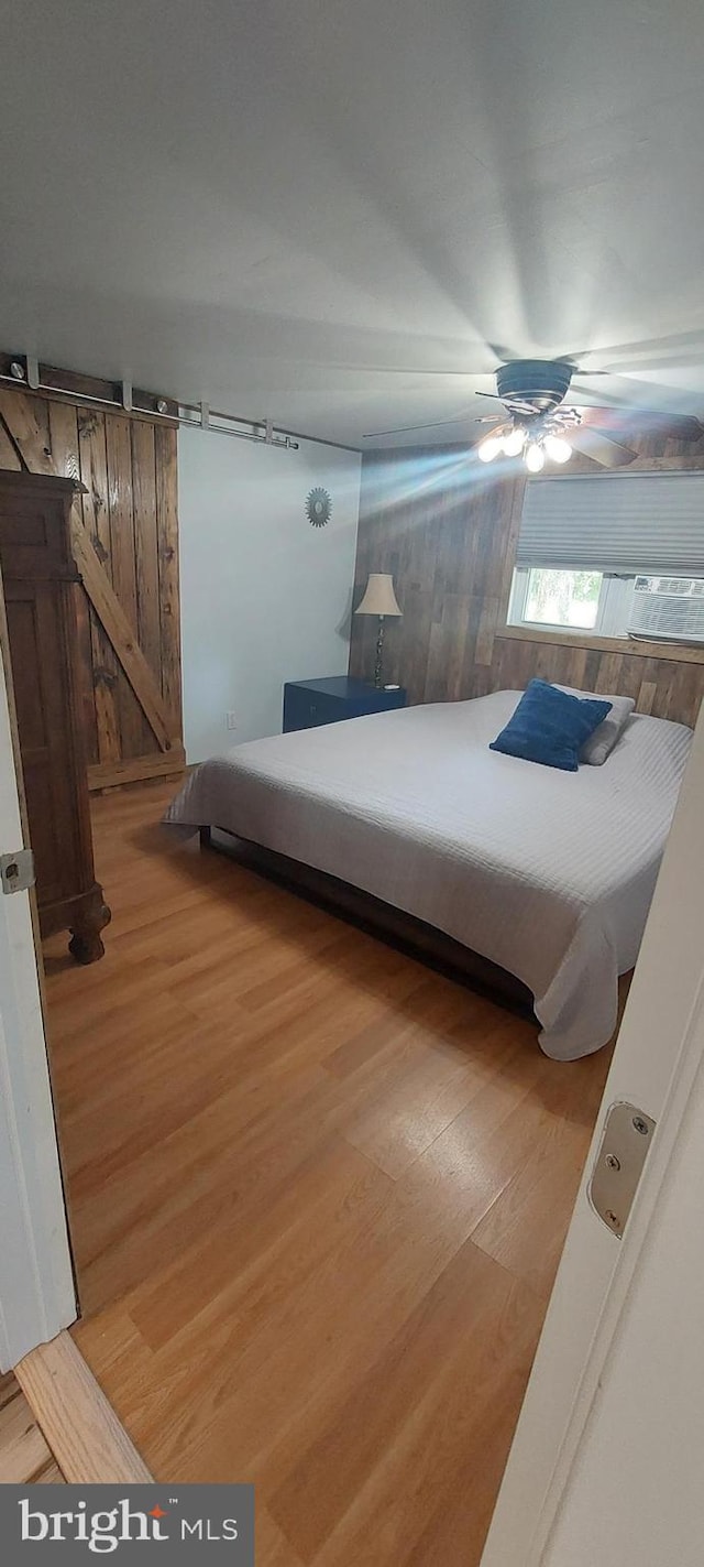 bedroom featuring a barn door, ceiling fan, and light wood-type flooring