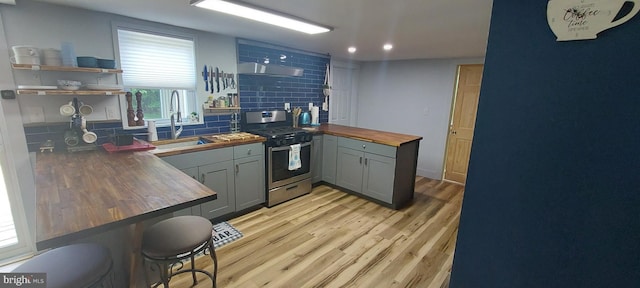 kitchen with sink, backsplash, gas stove, wood counters, and light wood-type flooring