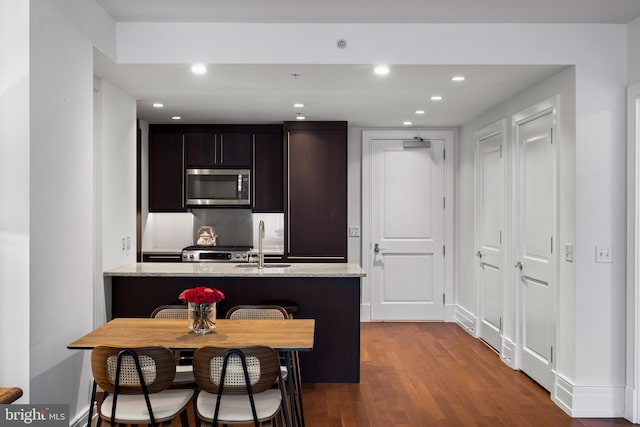 kitchen with light stone counters, a kitchen bar, sink, and hardwood / wood-style floors