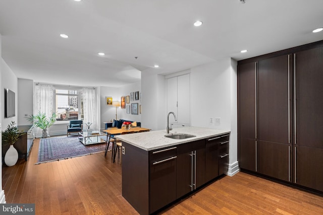 kitchen with light stone countertops, sink, light wood-type flooring, and kitchen peninsula