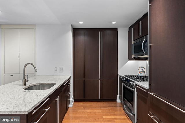 kitchen featuring appliances with stainless steel finishes, light stone countertops, sink, and light hardwood / wood-style flooring