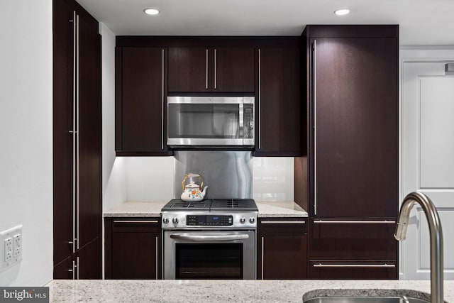 kitchen with stainless steel appliances, dark brown cabinets, sink, and light stone counters