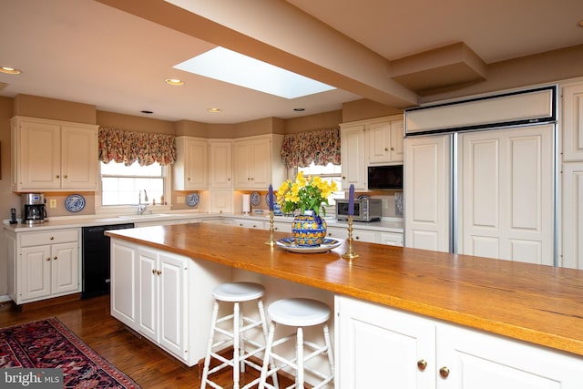 kitchen featuring butcher block counters, white cabinetry, a skylight, dark hardwood / wood-style floors, and black dishwasher