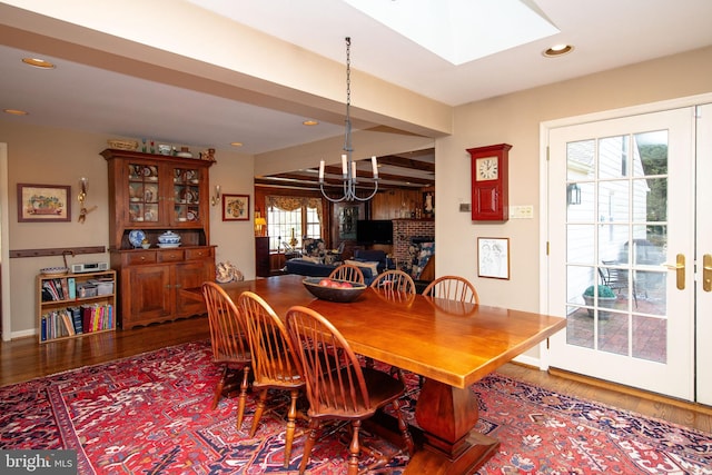 dining area featuring wood-type flooring, a brick fireplace, a notable chandelier, and a skylight