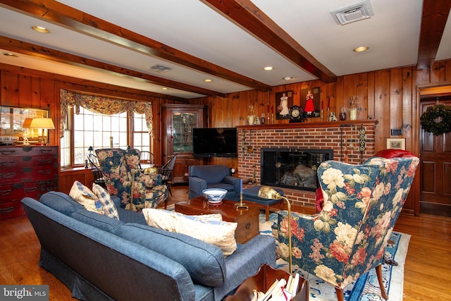 living room featuring hardwood / wood-style flooring, beam ceiling, a brick fireplace, and wood walls