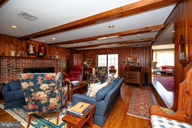 living room with hardwood / wood-style floors, beam ceiling, wooden walls, and a brick fireplace