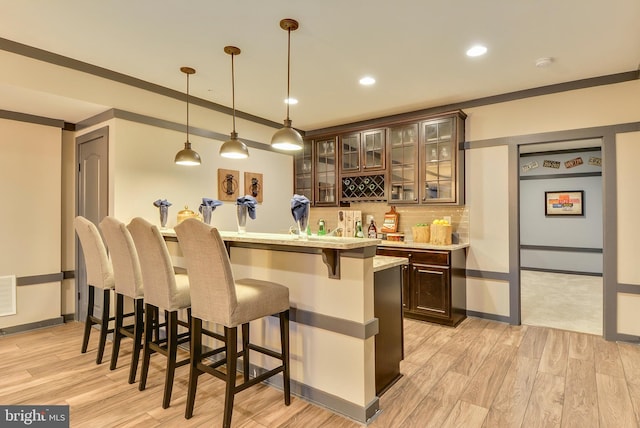 bar with decorative light fixtures, dark brown cabinets, light wood-type flooring, ornamental molding, and backsplash