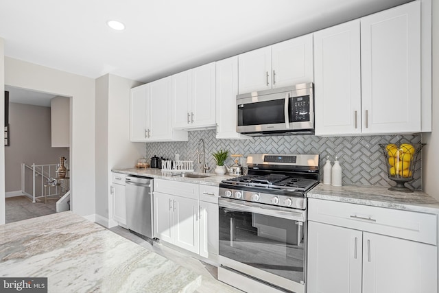 kitchen featuring stainless steel appliances, white cabinetry, light stone countertops, and sink