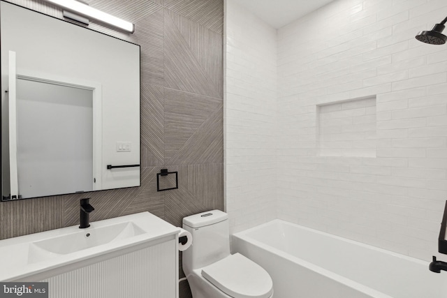 full bathroom featuring tiled shower / bath, vanity, toilet, and tile walls