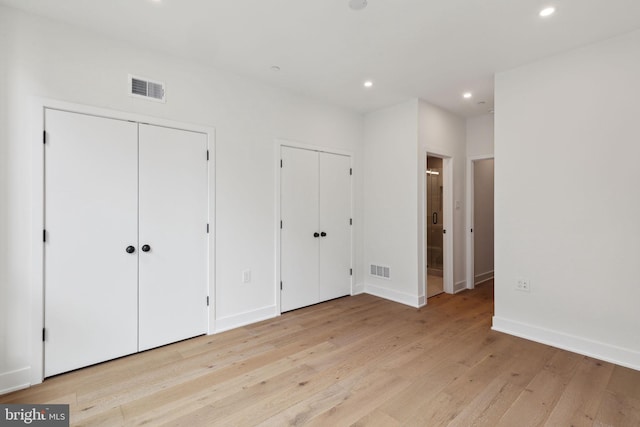 unfurnished bedroom with ensuite bath, multiple closets, and light wood-type flooring