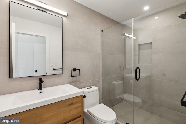 bathroom featuring walk in shower, vanity, toilet, and tile walls