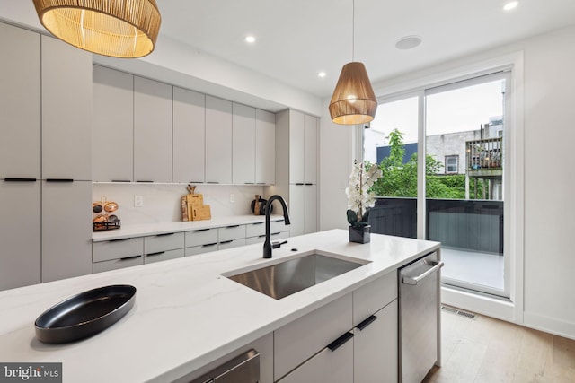 kitchen with pendant lighting, dishwasher, sink, light hardwood / wood-style floors, and light stone countertops