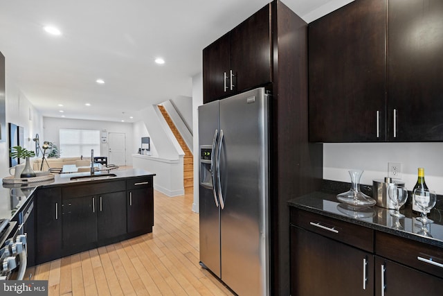 kitchen featuring dark brown cabinetry, sink, light wood-type flooring, dark stone countertops, and stainless steel appliances