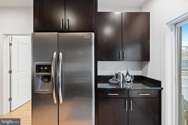 kitchen featuring light hardwood / wood-style flooring, dark stone countertops, dark brown cabinetry, and stainless steel fridge with ice dispenser