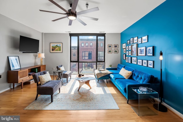 living area featuring a ceiling fan, expansive windows, baseboards, and wood finished floors