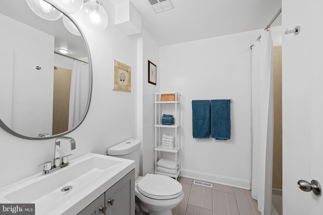 bathroom with toilet, vanity, visible vents, and baseboards