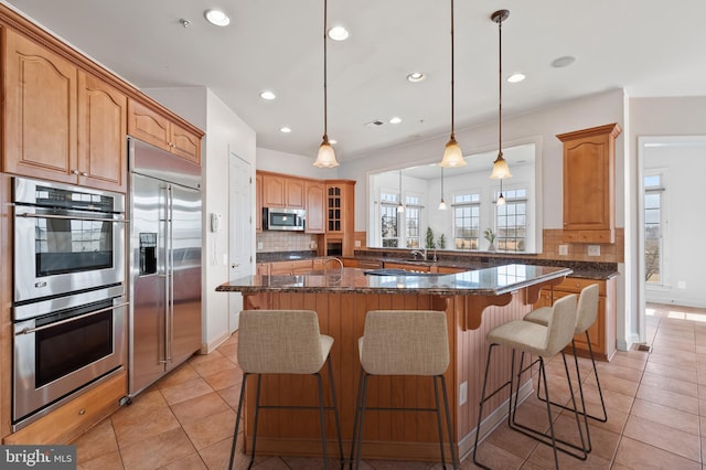 kitchen featuring light tile patterned floors, appliances with stainless steel finishes, backsplash, and a breakfast bar area