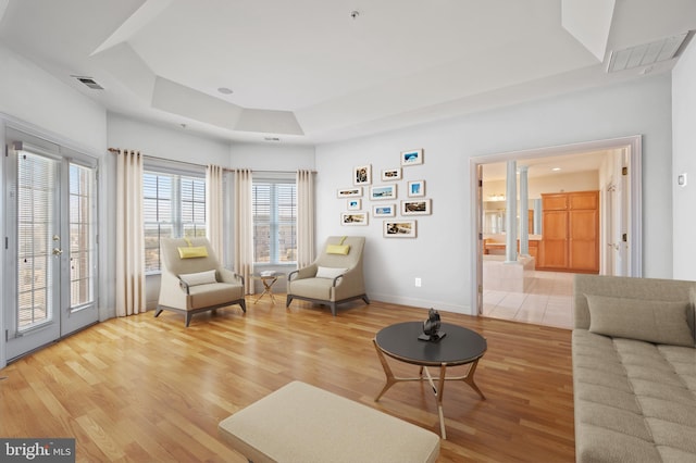 living area featuring light wood-style floors, a tray ceiling, visible vents, and baseboards