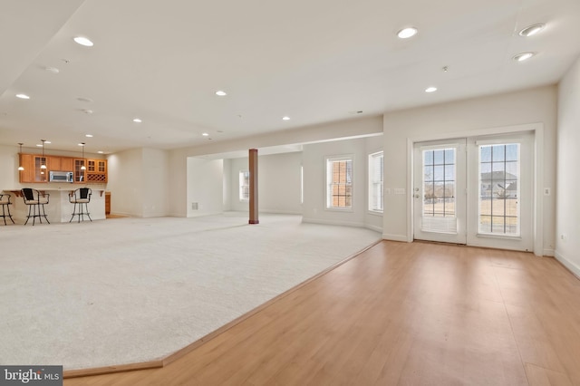 unfurnished living room with light carpet, light wood-type flooring, baseboards, and recessed lighting