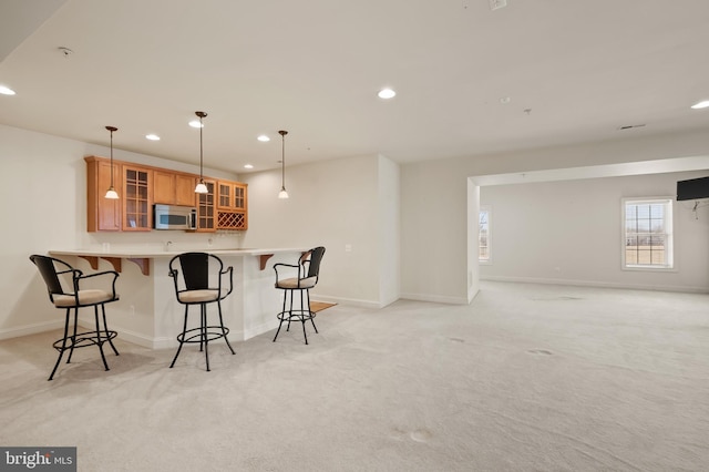 kitchen featuring brown cabinetry, recessed lighting, stainless steel microwave, and light carpet