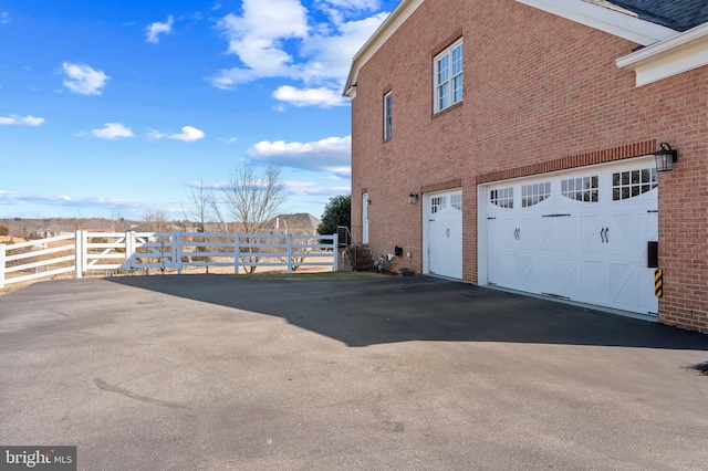 view of home's exterior with brick siding, fence, driveway, and an attached garage