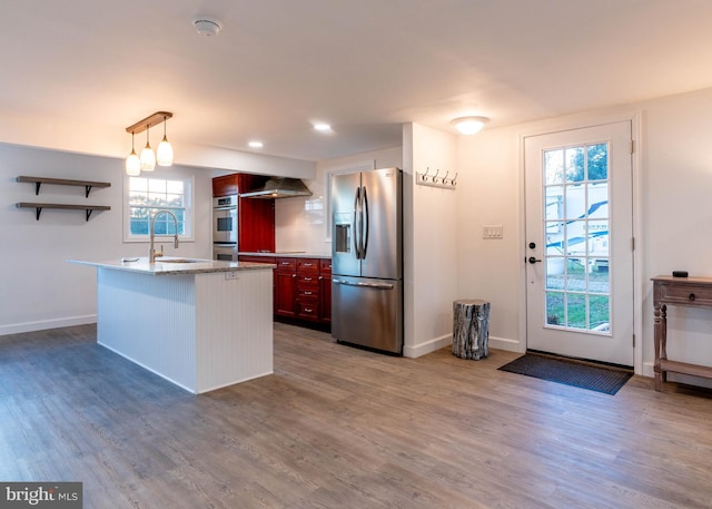 kitchen with appliances with stainless steel finishes, decorative light fixtures, sink, a center island with sink, and wall chimney exhaust hood