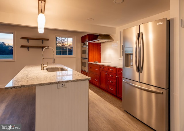 kitchen with wall chimney exhaust hood, sink, light stone counters, pendant lighting, and stainless steel appliances