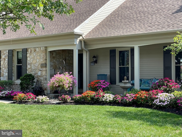 property entrance with stone siding, a shingled roof, and a lawn