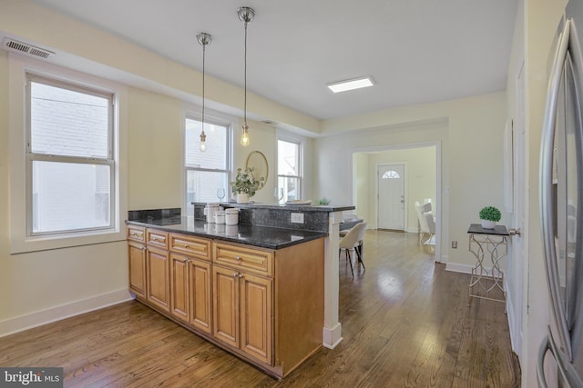 kitchen with brown cabinetry, wood finished floors, dark stone countertops, freestanding refrigerator, and pendant lighting