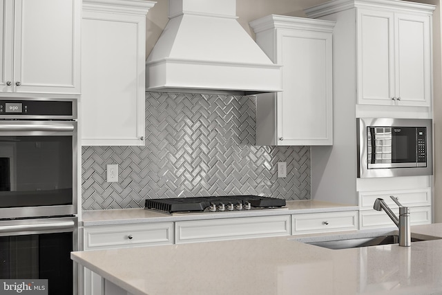 kitchen featuring white cabinets, a sink, stainless steel appliances, and premium range hood
