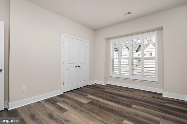 unfurnished bedroom featuring dark wood-type flooring, baseboards, visible vents, and a closet