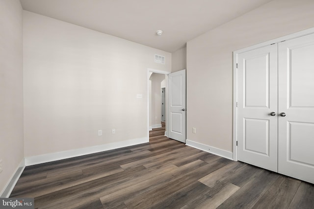unfurnished bedroom with dark wood-style floors, visible vents, and baseboards