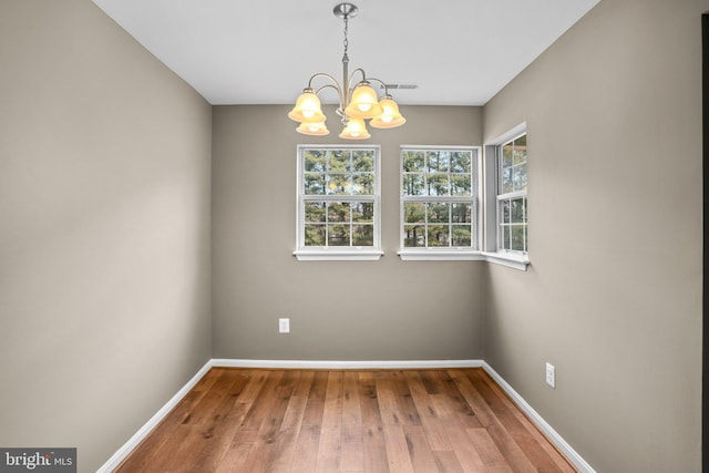 unfurnished dining area featuring a notable chandelier, wood finished floors, visible vents, and baseboards