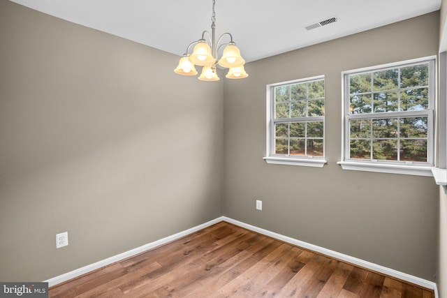 empty room featuring a chandelier, wood finished floors, visible vents, and baseboards