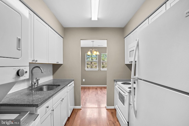 kitchen with stacked washer and dryer, white appliances, a sink, white cabinets, and light wood-type flooring