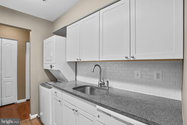 kitchen featuring a sink, stacked washer / drying machine, white cabinets, decorative backsplash, and dark wood finished floors