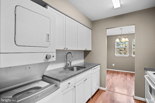 kitchen featuring stacked washer / drying machine, white appliances, white cabinetry, and a sink